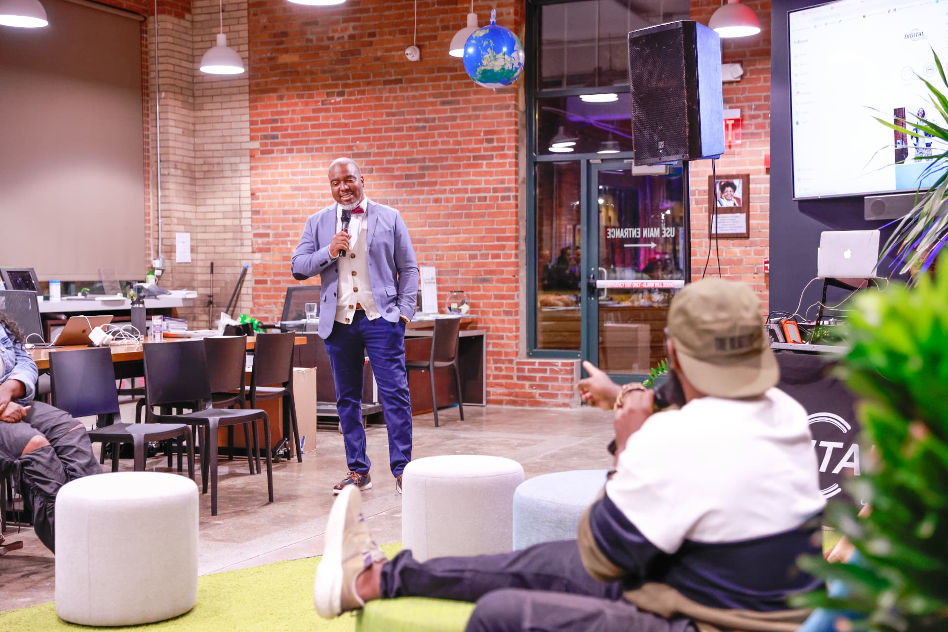 Jay.R Fogle speaking to a relaxed audience in a brick-walled coworking space